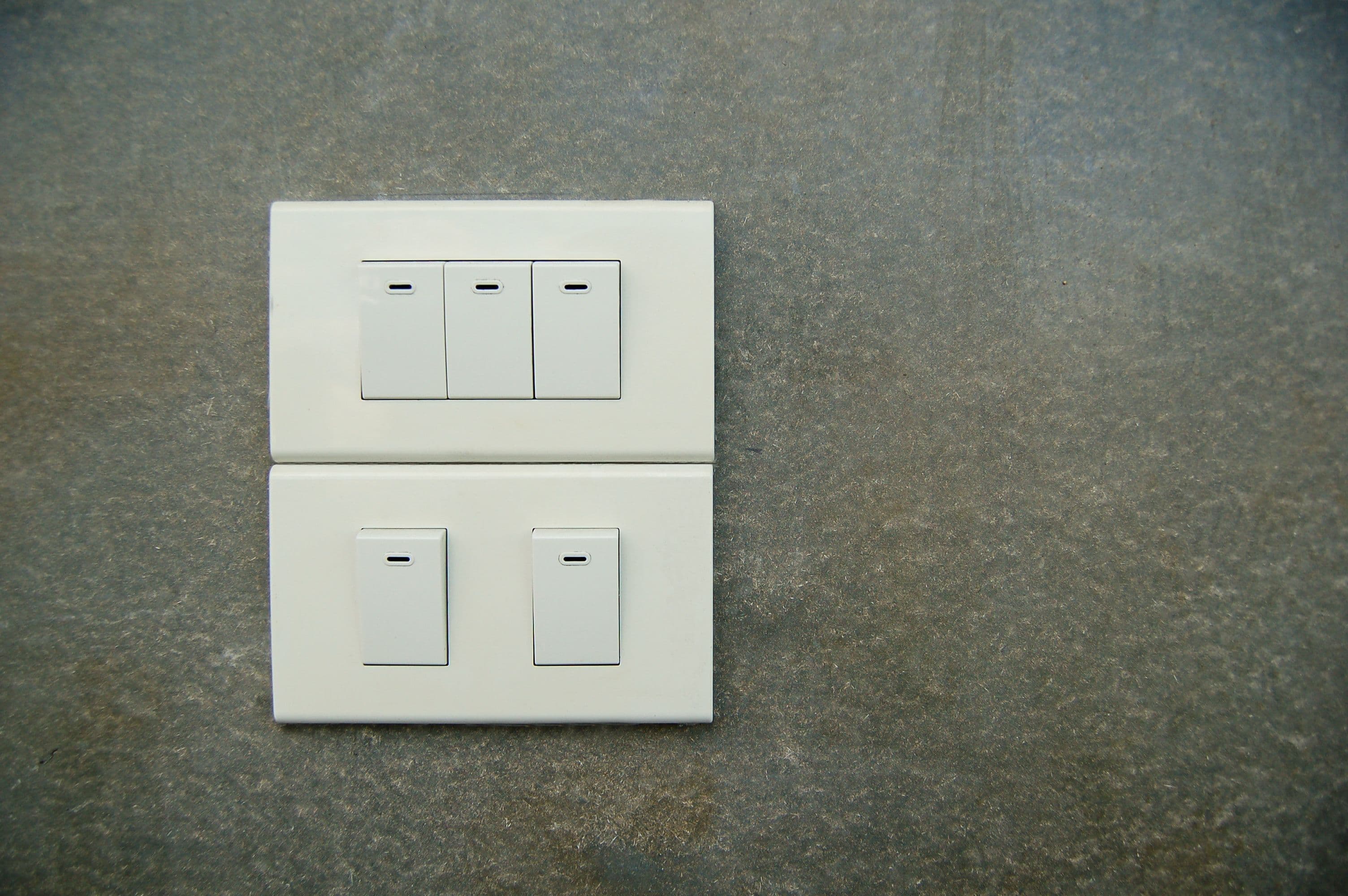 Minimalist photo of white electrical rocker switches on a textured stone wall background.